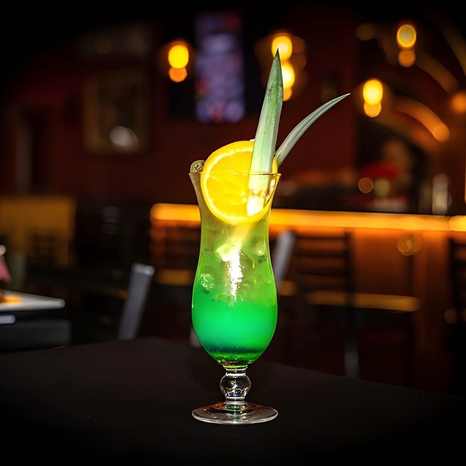 Vibrant green Caribbean cocktail with an orange slice and pineapple leaf garnish on a dark table.
