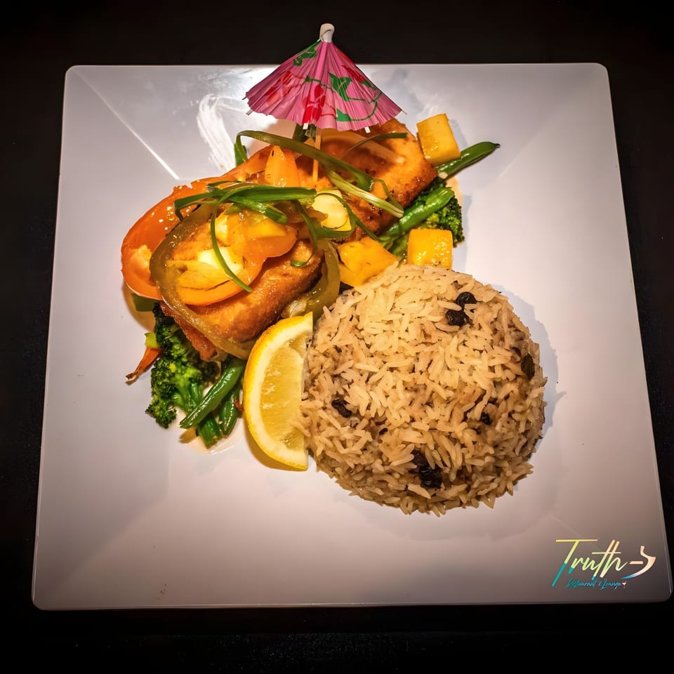 Truth Restaurant's Caribbean dish with fish, rice and peas, vegetables, and a pink cocktail umbrella.