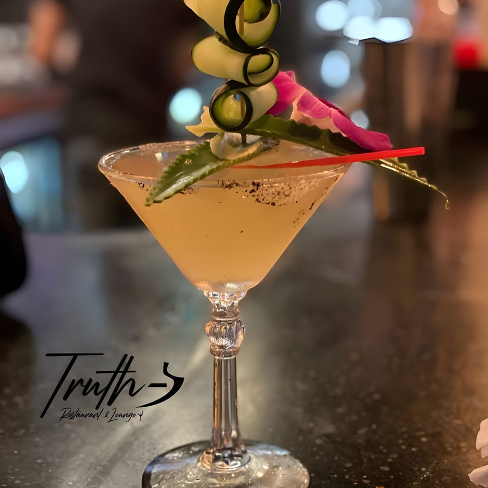 A Caribbean cocktail garnished with cucumber slices, a pink orchid, and a red straw.