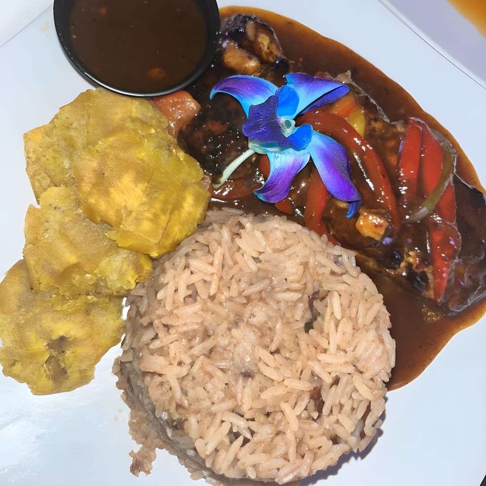 Caribbean stewed chicken with rice, fried plantains, and a blue orchid garnish on a white plate.