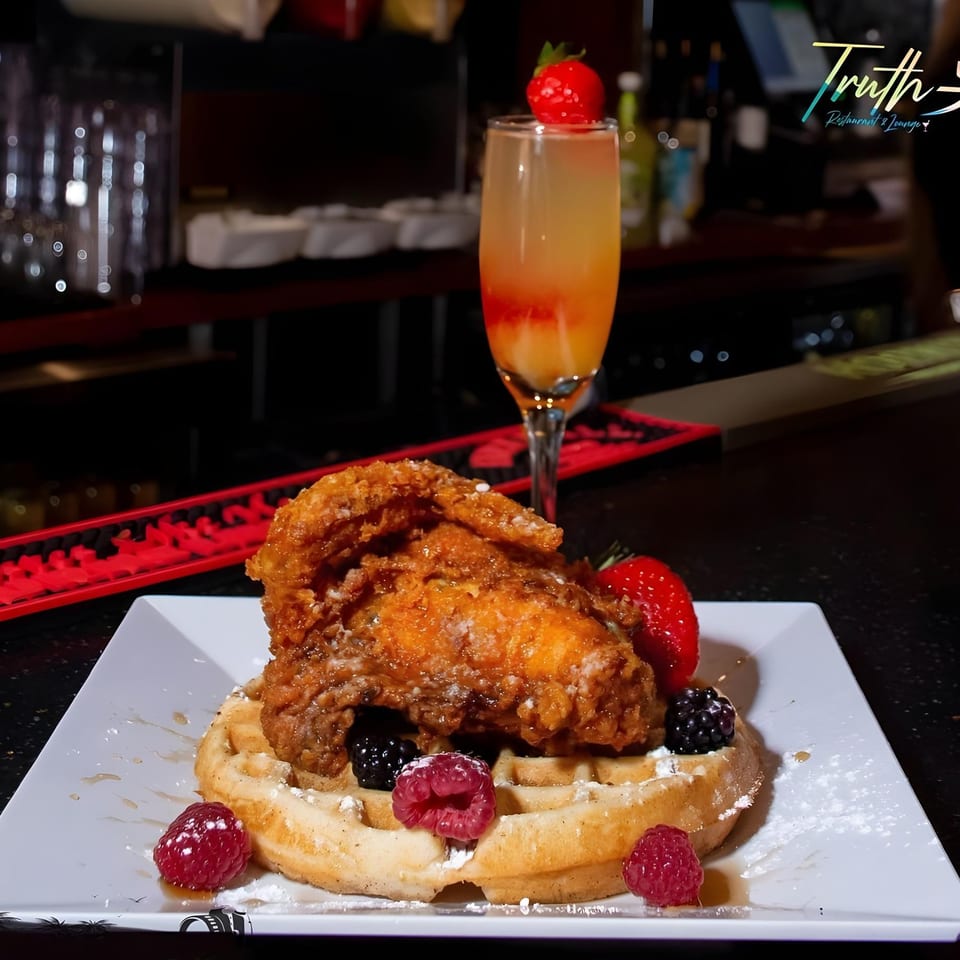 Crispy fried chicken and waffle with berries and powdered sugar, alongside a mimosa at Truth Restaurant.