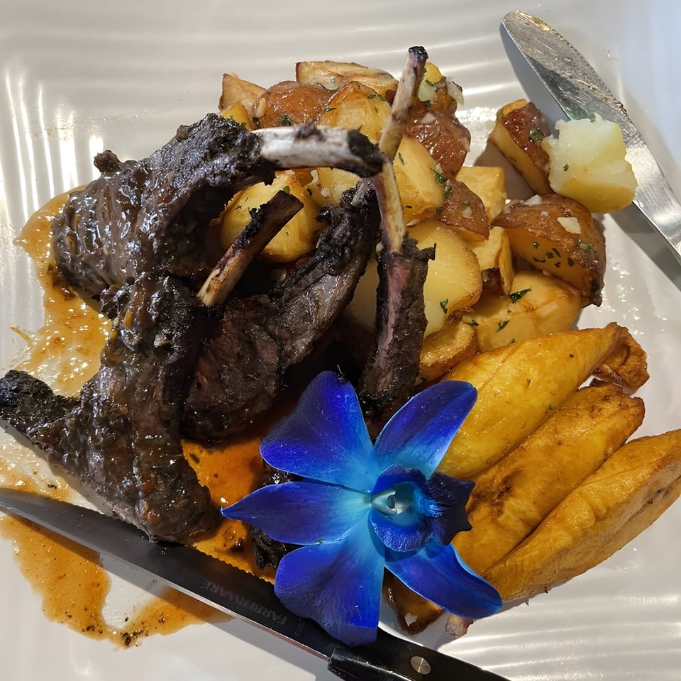 Caribbean lamb chops with roasted potatoes, fried plantains, and a blue orchid garnish.