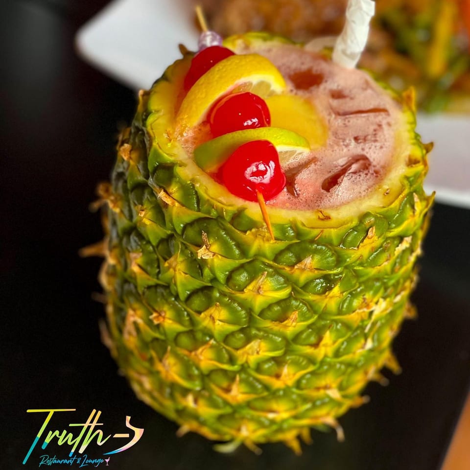A vibrant Caribbean cocktail served in a hollowed-out pineapple, garnished with cherries and citrus slices.